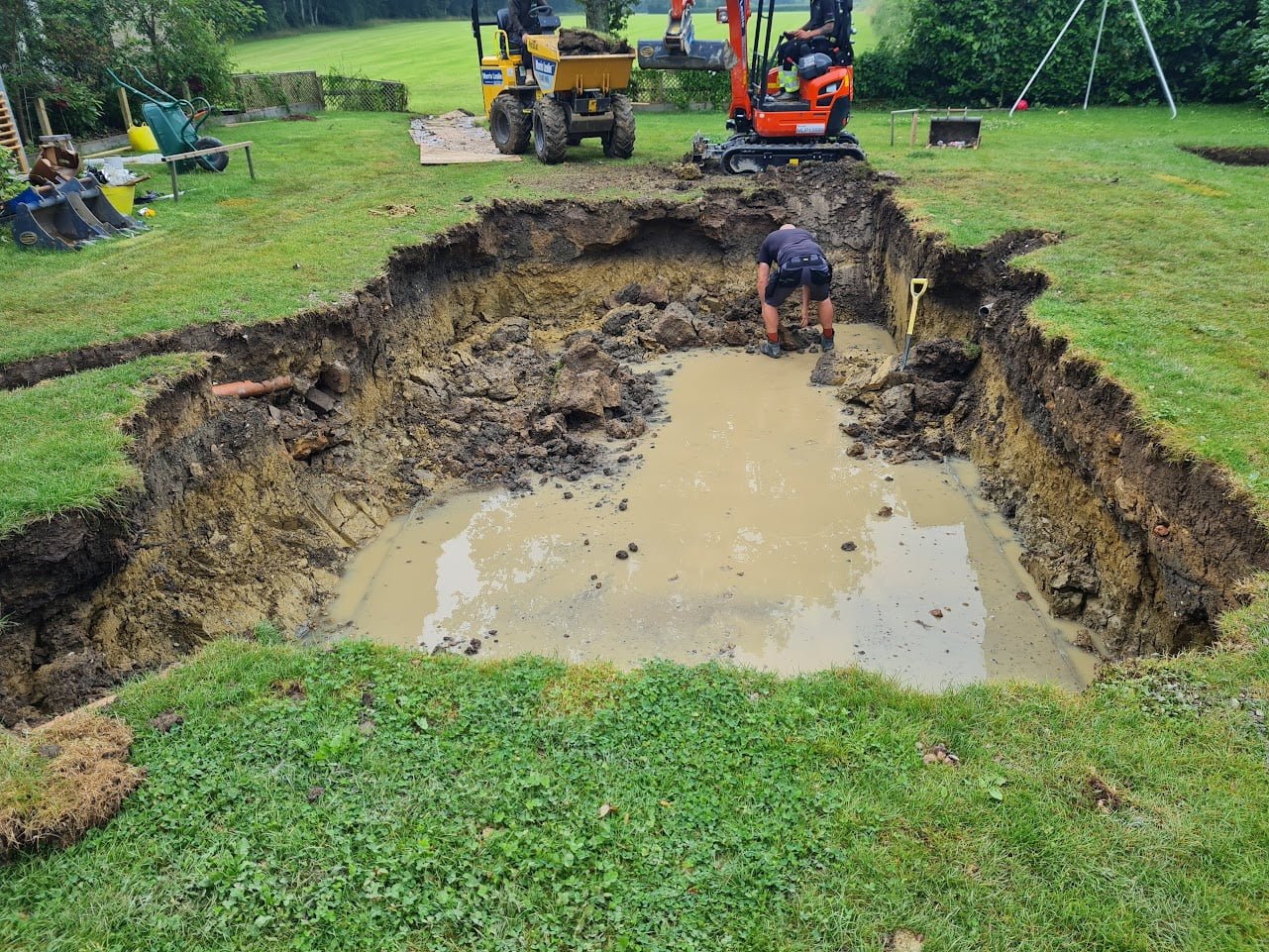 Rectangle shaped pool being dug in a garden with an industrial digger